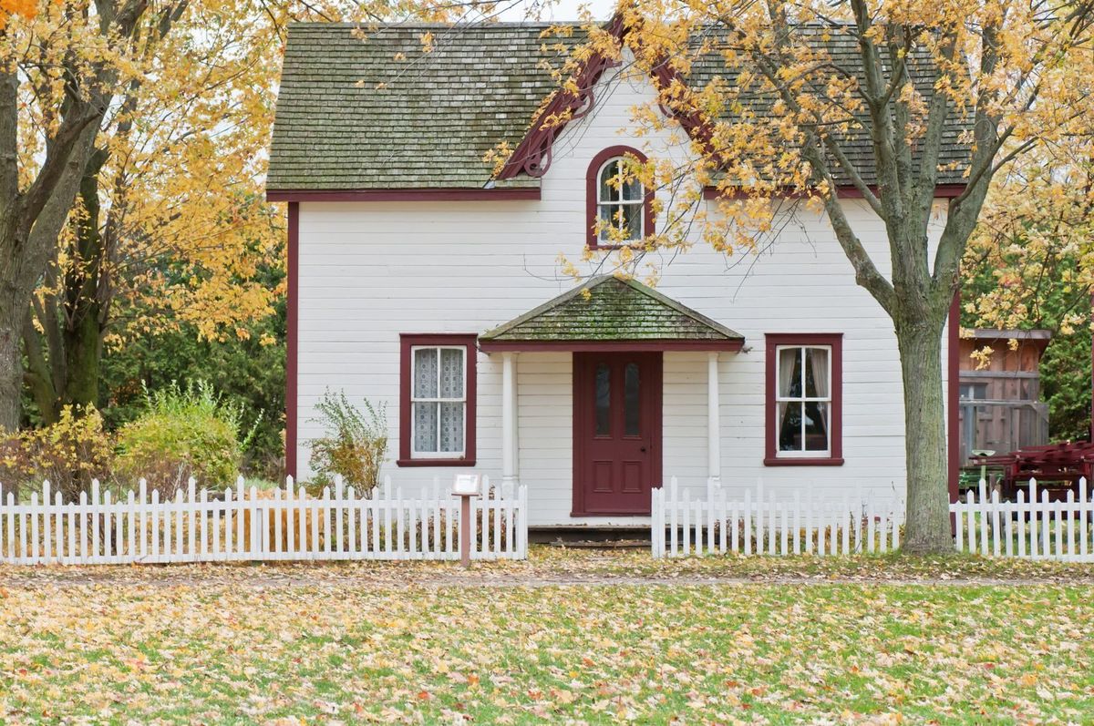 A two-story house with a shingled roof, autumn trees and fallen leaves on the lawn